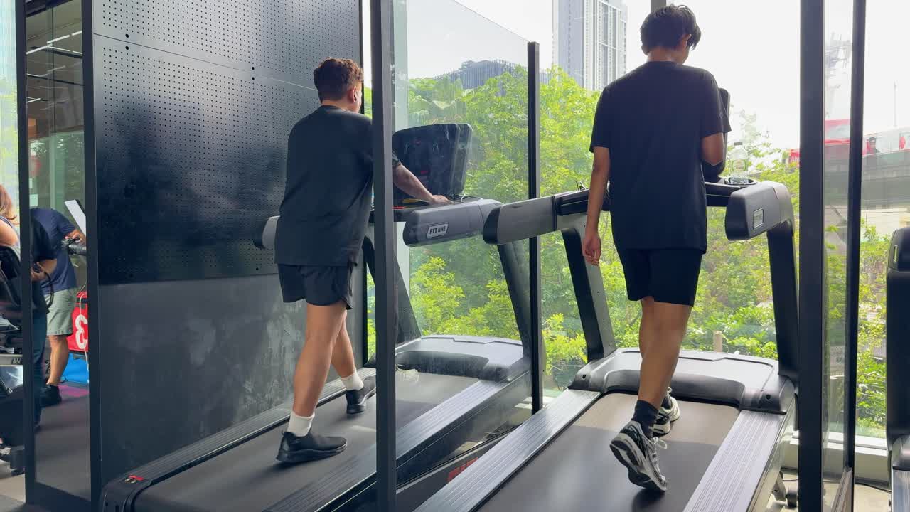 A person exercises on a treadmill in a gym with large windows overlooking a lush, urban landscape