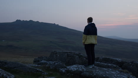 dartmoor, devon, england, uk, a man stands atop a rocky hill, gazing out at the serene, expansive landscape bathed in the warm hues of sunset, medium shot