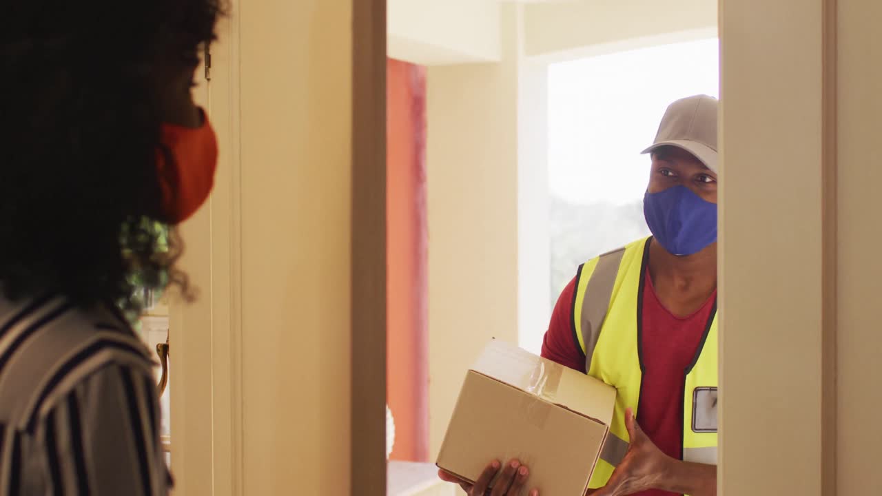 Delivery man wearing face mask delivering package to african american woman wearing face mask at hom