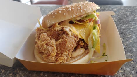 a mexican-inspired burger with crispy chicken slice, cheese, and taco flavors served on a table inside a fast-food restaurant.