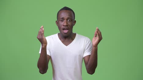 young african man looking shocked against green background