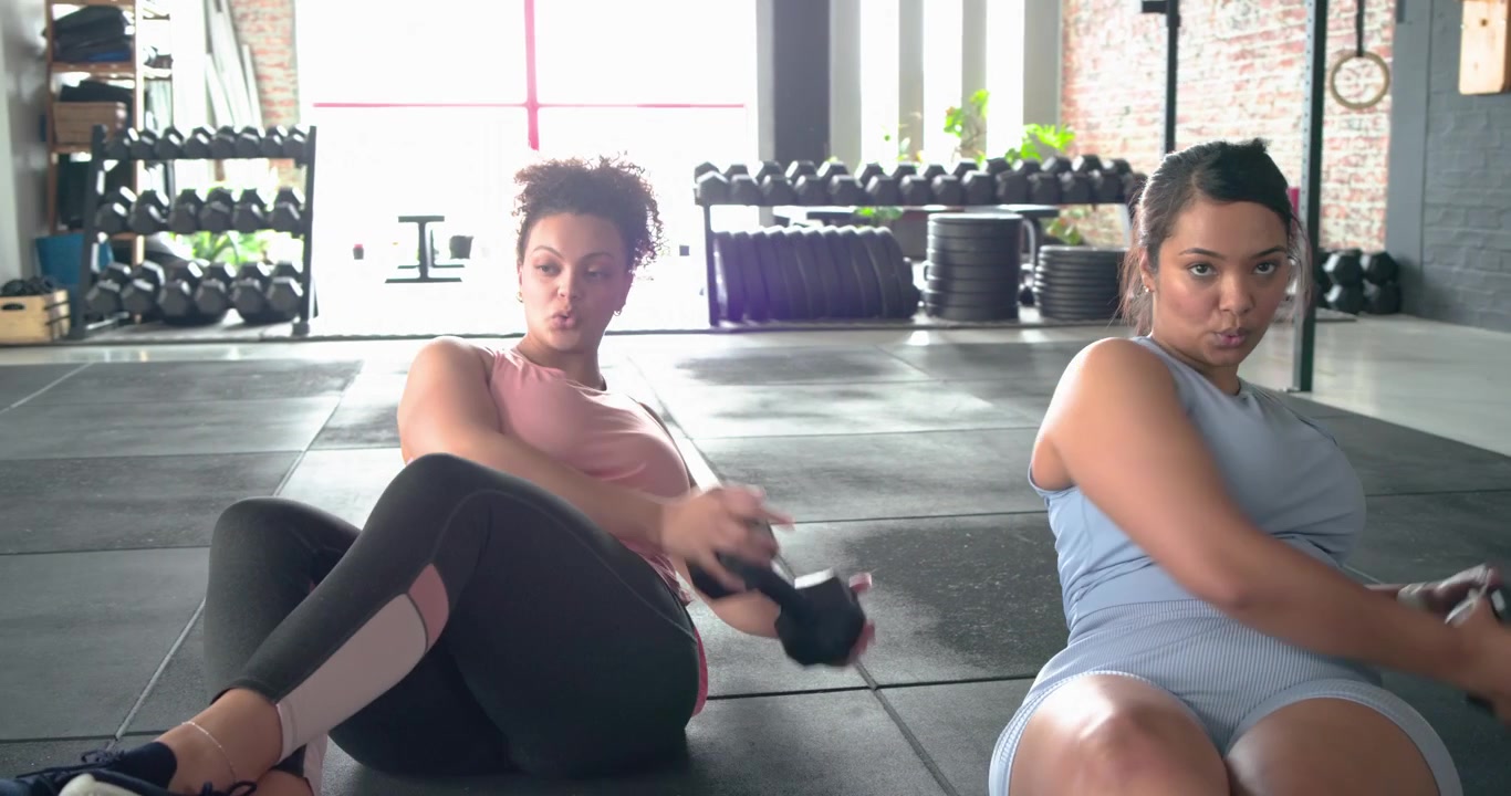 After warming up diverse women twisting weights at gym to tone core and clasping hands