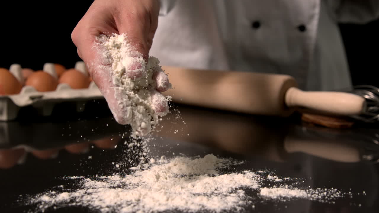 Chef sprinkling flour on black surface