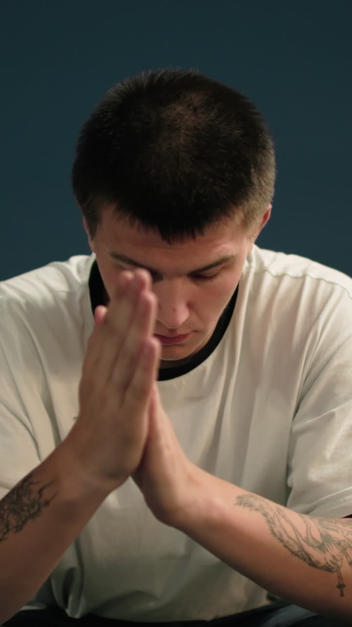 색 폴로 옷을 입은 젊은이가 손으로 얼굴을 고 손을 는 동안 손을 제거하고, 조용한 도시 환경에서 반사와 감정을 표현하는 배경에 streetlamps를 조명합니다.