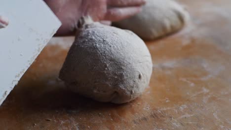 puffy ball of dough shaped and shuffled using scraper tool on wooden kitchen tabletop, filmed as extreme closeup in slow motion shot