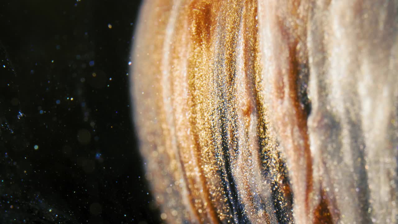 황금 잉크 입자는 검은 바탕에 다채로운 혼란으로 물에 흐른다.