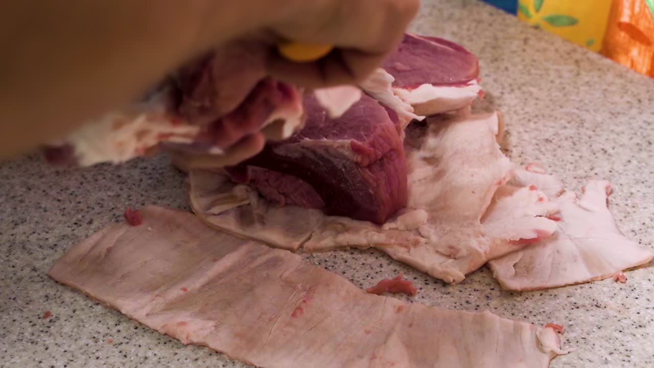 quitar la piel de los trozos de carne de cerdo fresca en la cocina doméstica, vista de cerca