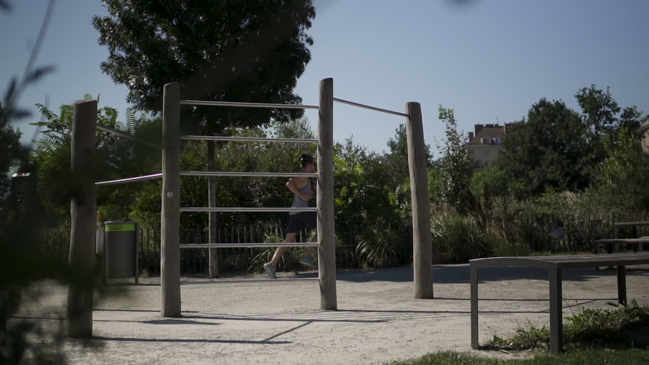 un hombre corriendo por un parque lleno de equipos de gimnasia en cámara lenta durante un entrenamiento