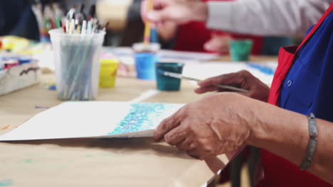 senior woman with friends attending art class in community centre painting picture