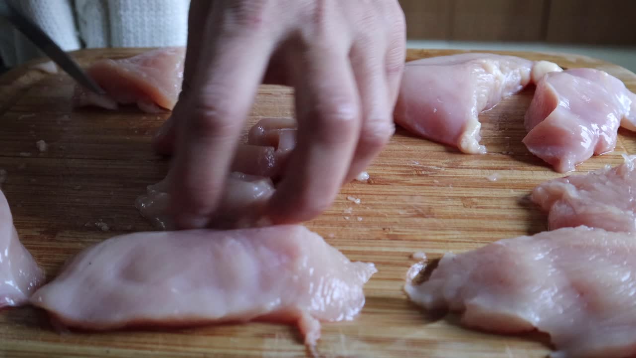 cocine cortando carne de pollo fresca en tiras usando un cuchillo afilado en una tabla de madera - ángulo alto, de cerca