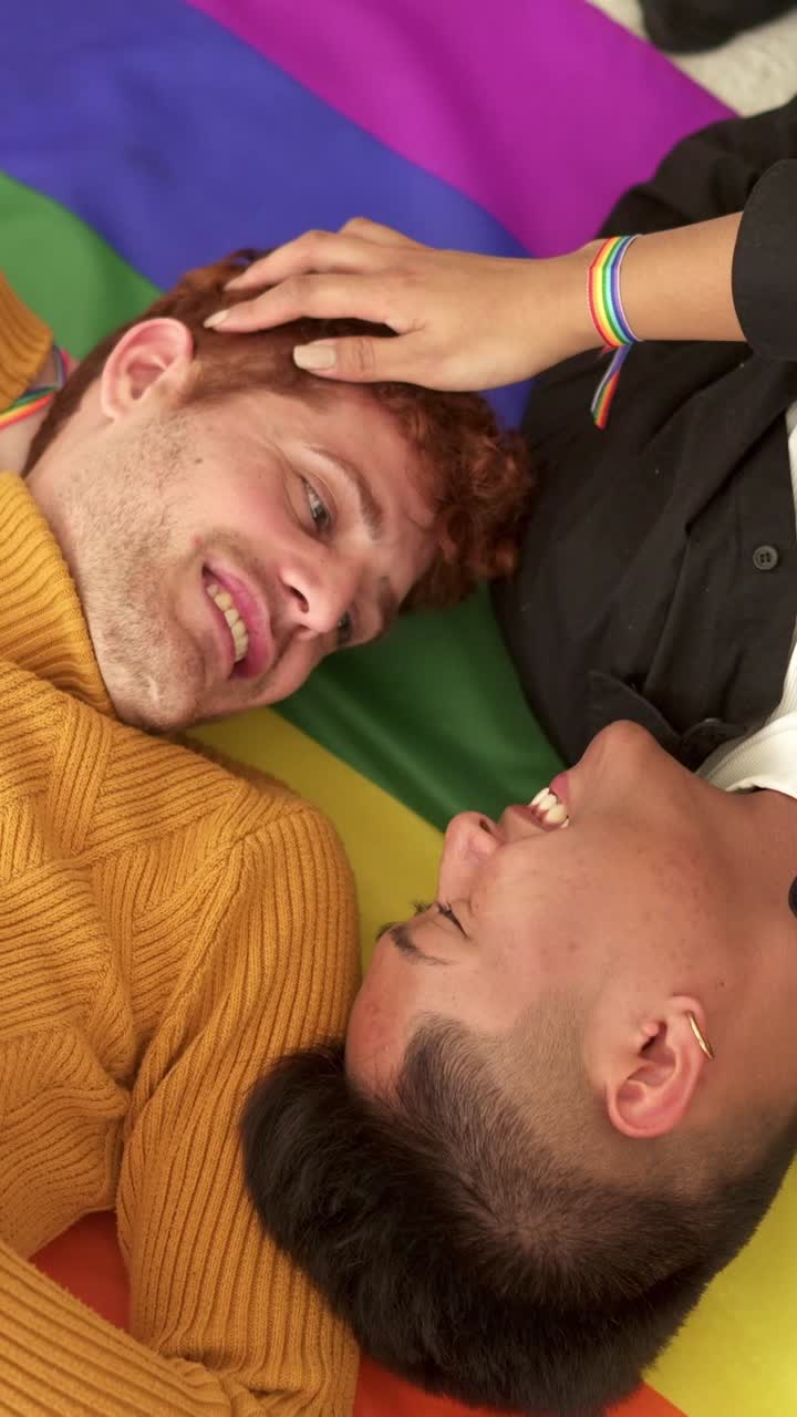 Happy LGBTQ+ couple smiling and looking at each other on a rainbow flag