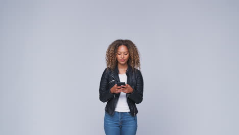 Studio-Shot-Of-Woman-Wearing-Leather-Jacket-Sending-Text-Message-On-Mobile-Phone-In-Slow-Motion