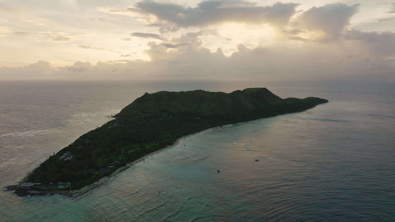 Large tropical island under overcast sky with turquoise water and distant reef