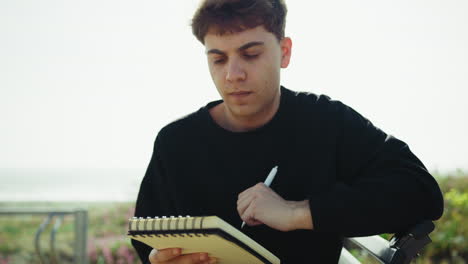 man writing ideas on a notebook with a pen on a park bench