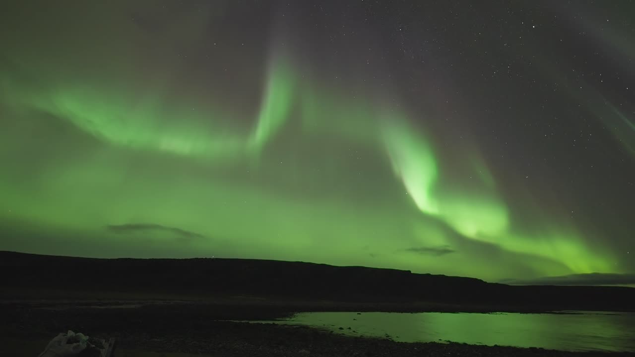 en una oscura noche de invierno, un fiordo tranquilo está iluminado por la encantadora danza de las luces del norte en este video timelapse