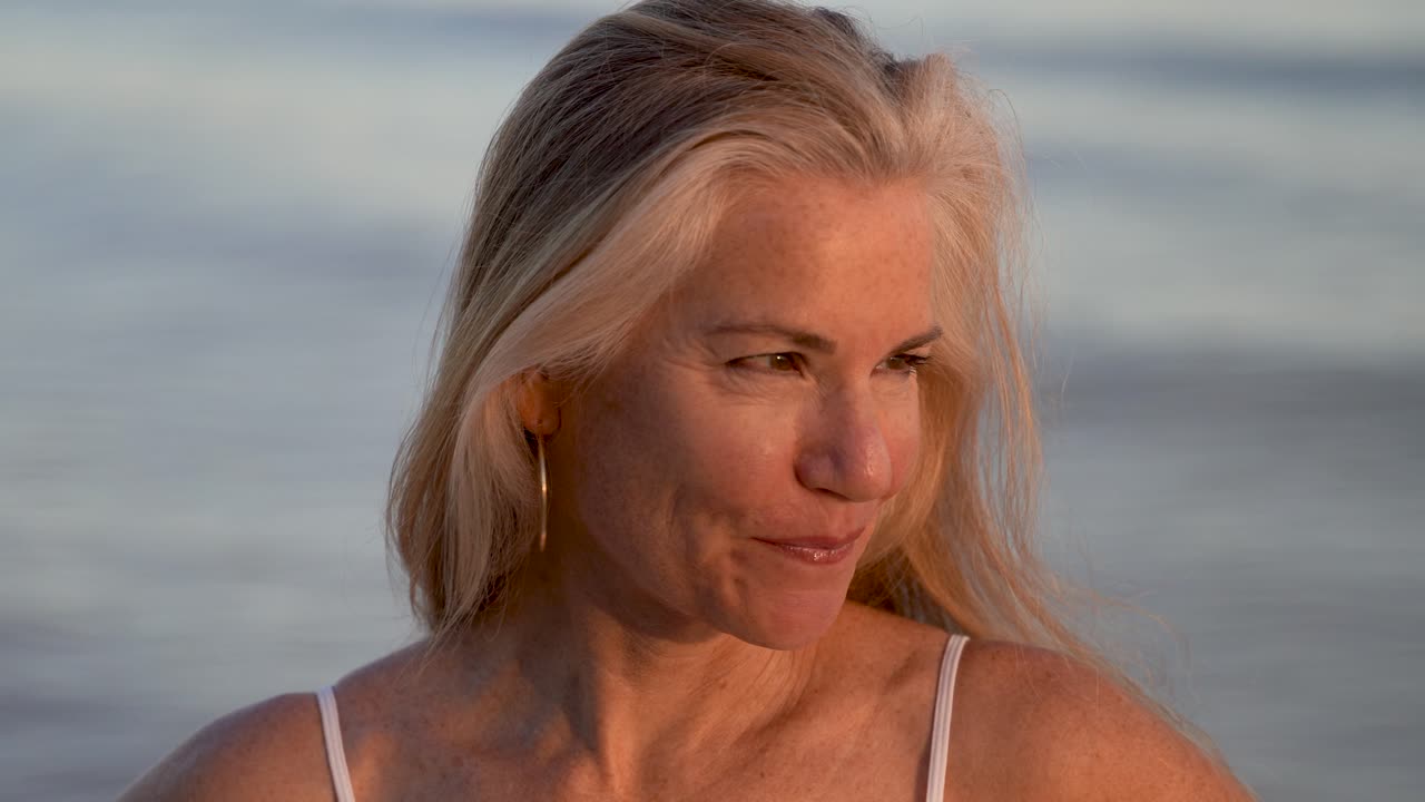 Beautiful mature blonde woman raising her arms looking into the setting sun and then looking at camera