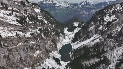 A-magnificent-aerial-view-captures-the-enchanting-beauty-of-snow,-lake,-and-mountains-at-Tahlalpsee,-Filzbach,-Glarus-Nord,-Switzerland