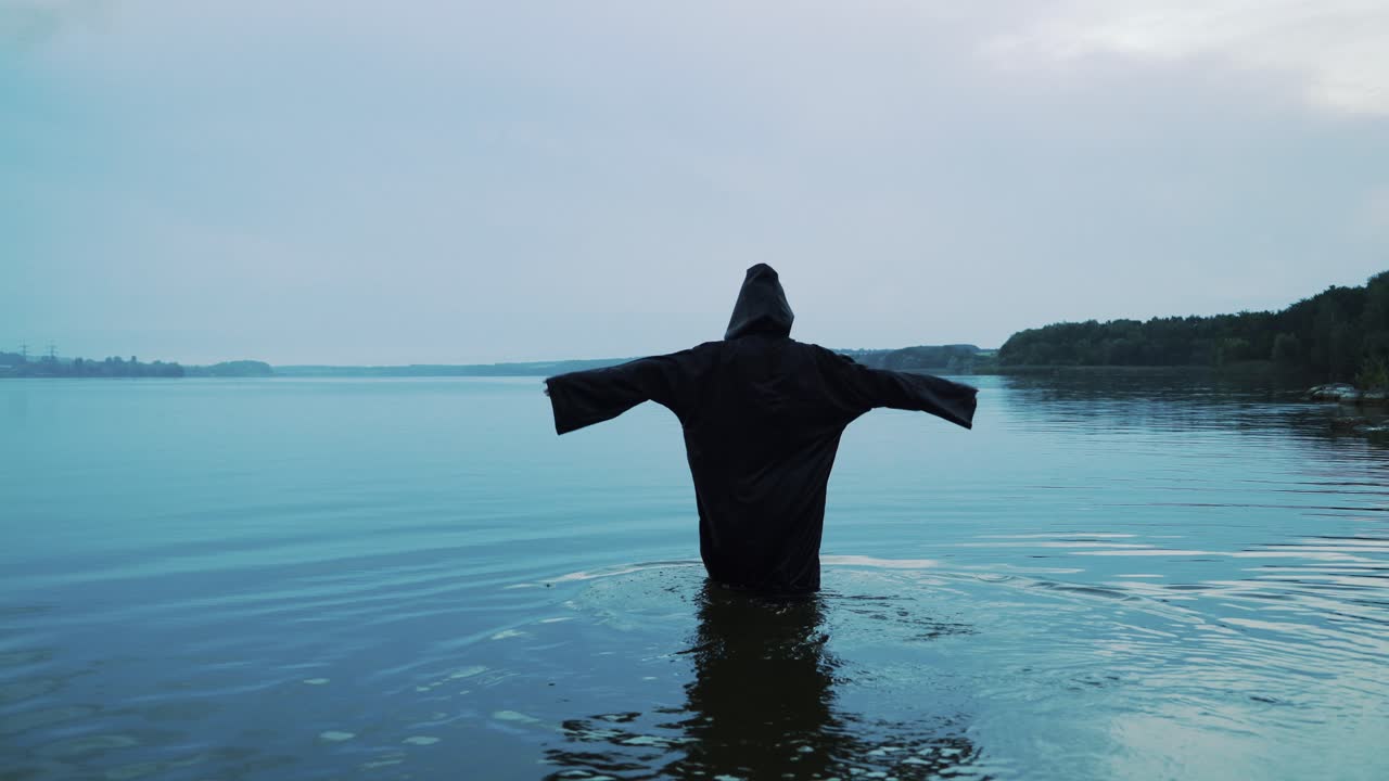 Female figure in a black robe enters the water. Halloween costume