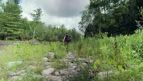 Lone-male-hiker-walking-through-rocky-overgrown-landscape-with-lush-green-foliage