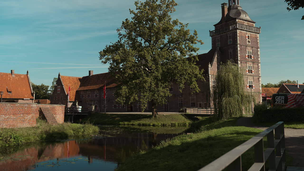 Wide shot of Schloss Raesfeld’s church complex with medieval architecture reflected in surrounding water, captured on a warm, sunny summer day