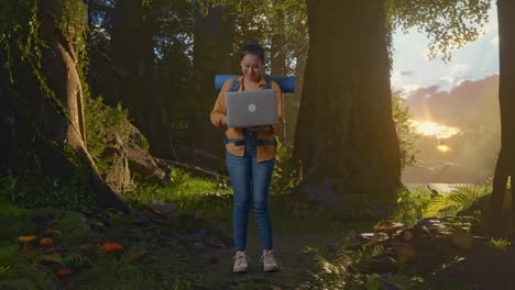 cuerpo lleno de excursionista femenina asiática con mochila de montañismo mirando una computadora portátil y gritando meta celebrando el éxito mientras explora la naturaleza del bosque