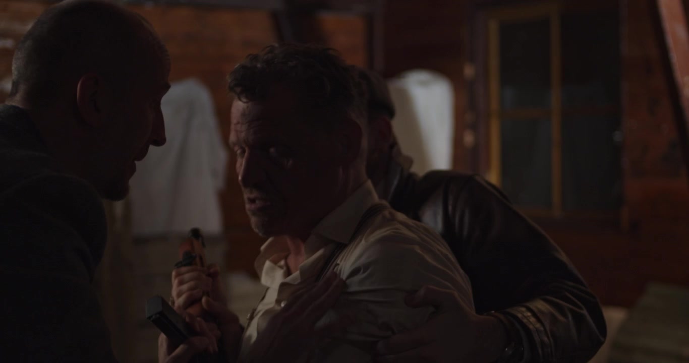 A man struggles to hold back a gangster carrying a Thompson sub machine gun. A partner jumps in and they send away the mad man