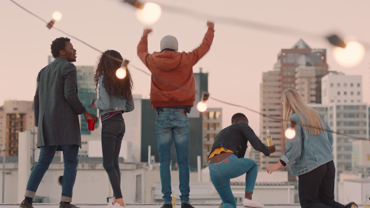 diverse group of friends on rooftop celebrating friendship with arms raised enjoying hanging out together drinking alcohol embracing freedom looking at beautiful city skyline at sunset