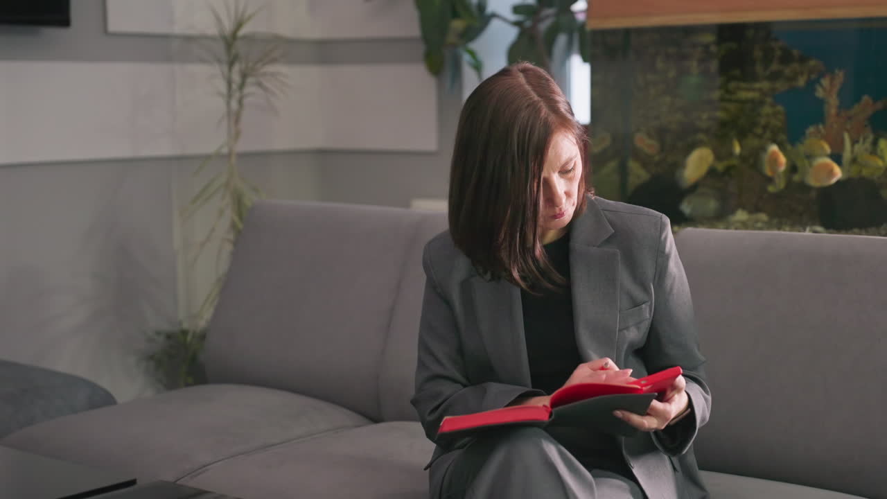 Bizneswoman czyta notatnik w nowoczesnym biurze, pogrążona w myślach, pracuje nad planami, środowisko korporacyjne, szary garnitur, profesjonalny strój, przerwa w pracy, koncentracja, produktywność