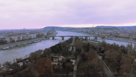 autumnal trees in margaret island with arpad bridge at danube river in budapest, hungary - drone pullback