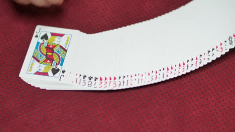 slow motion closeup of a a deck of cards being spread on a red game table