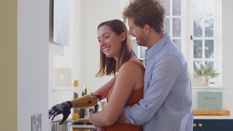 pareja amorosa con mujer con brazo protésico en la cocina preparando comida juntos y abrazándose