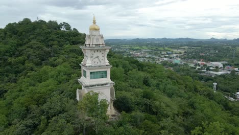 clock tower nestled on a hill amongst forest trees in thailand