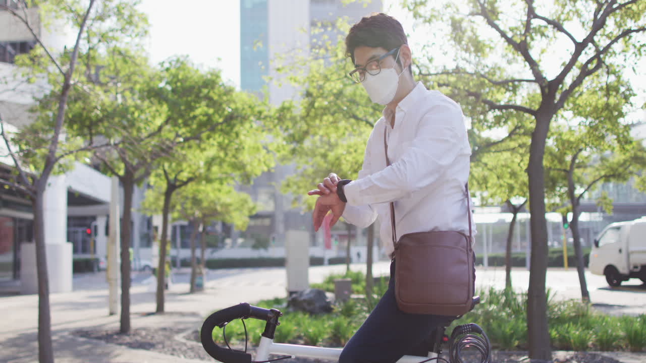 Asian man wearing face mask using smartwatch while sitting on his bicycle on the street