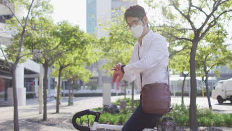 asian man wearing face mask using smartwatch while sitting on his bicycle on the street