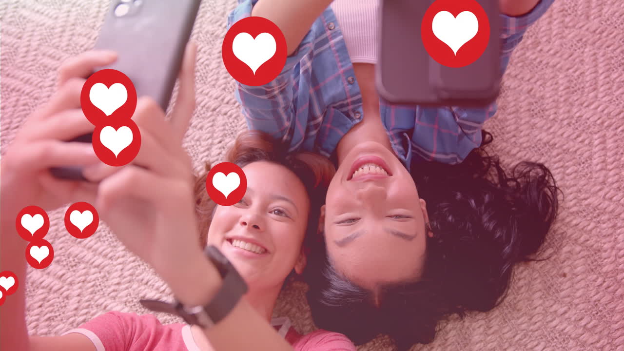 Taking selfies and smiling, two women with heart icons animation over them