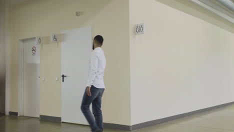 Man Walking in a Corridor Past Restrooms