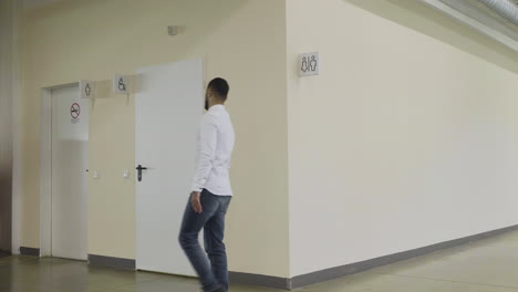 man walking in a corridor past restrooms