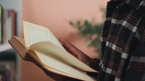 man flips page in book at college library. black student engrossed in reading literature in information center preparing for tests. customer in bookshop