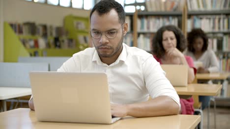 hombre afroamericano enfocado que usa una computadora portátil en la biblioteca