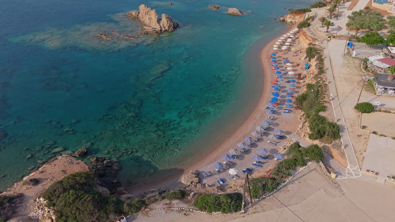 Top-down aerial view of Big Amopi Beach in Karpathos, showing beach loungers, golden sand, turquoise waters, and the stunning horizon