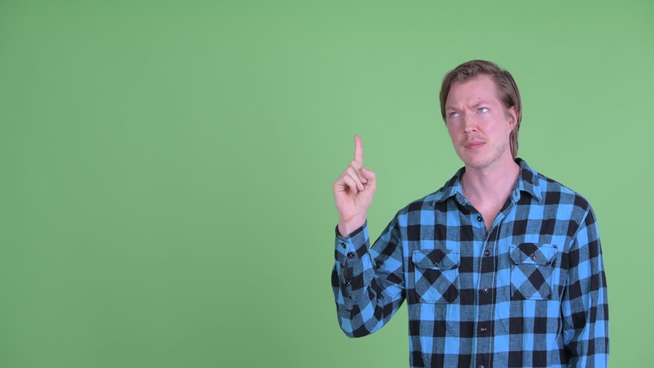 Ritratto di uomo caucasico dall'aspetto triste e frustrato mentre indica con il dito uno spazio per il testo, ripreso su sfondo verde da studio