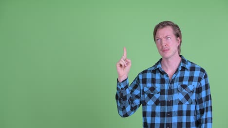retrato de un hombre caucásico mirando triste y frustrado mientras señala con el dedo para copiar el espacio disparado contra el fondo verde del estudio