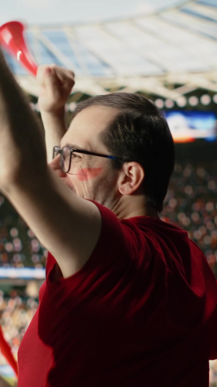 Video verticale. Vista posteriore di appassionati tifosi di calcio con maglie rosse che esultano nello stadio.