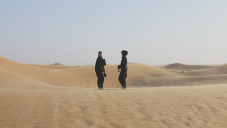 dos hermosas mujeres musulmanas en hiyab de pie en un desierto ventoso y sonriendo a la cámara 3