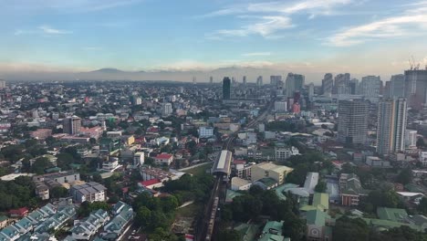 vuelo aéreo sobre un barrio suburbano de la ciudad de manila con trenes y rascacielos en el fondo a la hora del atardecer, filipinas