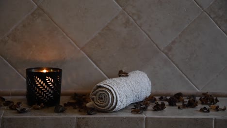 relaxing-spa-background-with-an-hidden-candle-with-flickering-flame,-some-wooden-petals-and-a-towel