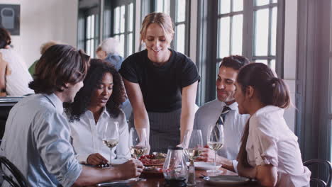 Camarera-Sirviendo-Comida-A-Compañeros-De-Trabajo-Sentados-Alrededor-De-La-Mesa-Del-Restaurante