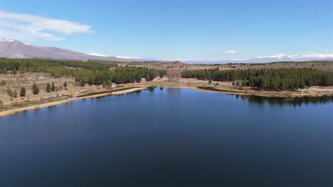 aerial view of the esquel lagoon la zeta reflecting the surrounding nature and mountains in patagonia, argentina, on a sunny day with blue sky