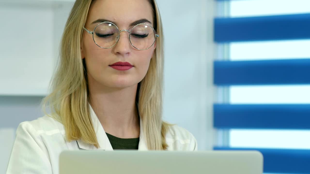 médica concentrada con gafas trabajando en una computadora portátil en el mostrador de recepción