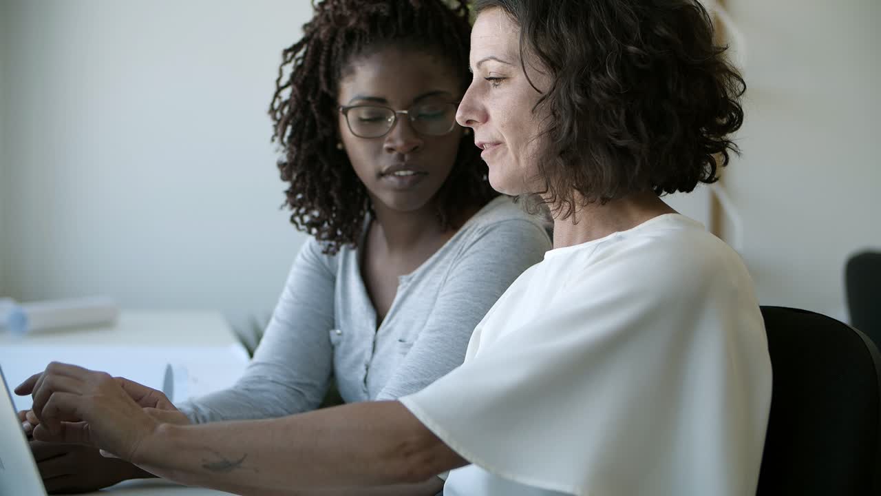 Two confident women talking while working with laptop